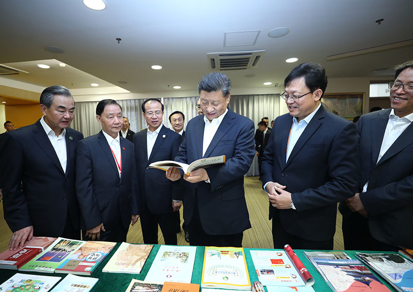 12月19日，國家主席習近平在澳門特別行政區行政長官崔世安陪同下，來到位於澳門黑沙環的政府綜合服務中心和濠江中學附屬英才學校，同澳門市民和師生親切交流。這是習近平在濠江中學附屬英才學校圖書館仔細翻看展台上擺放的教材。 新華社記者 鞠鵬 攝